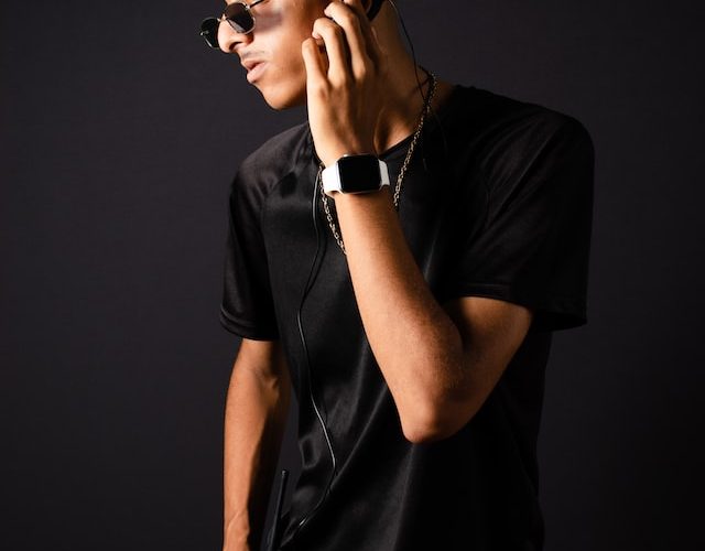 man with black hair and shades and black casual clothes looking at the side on a black background
